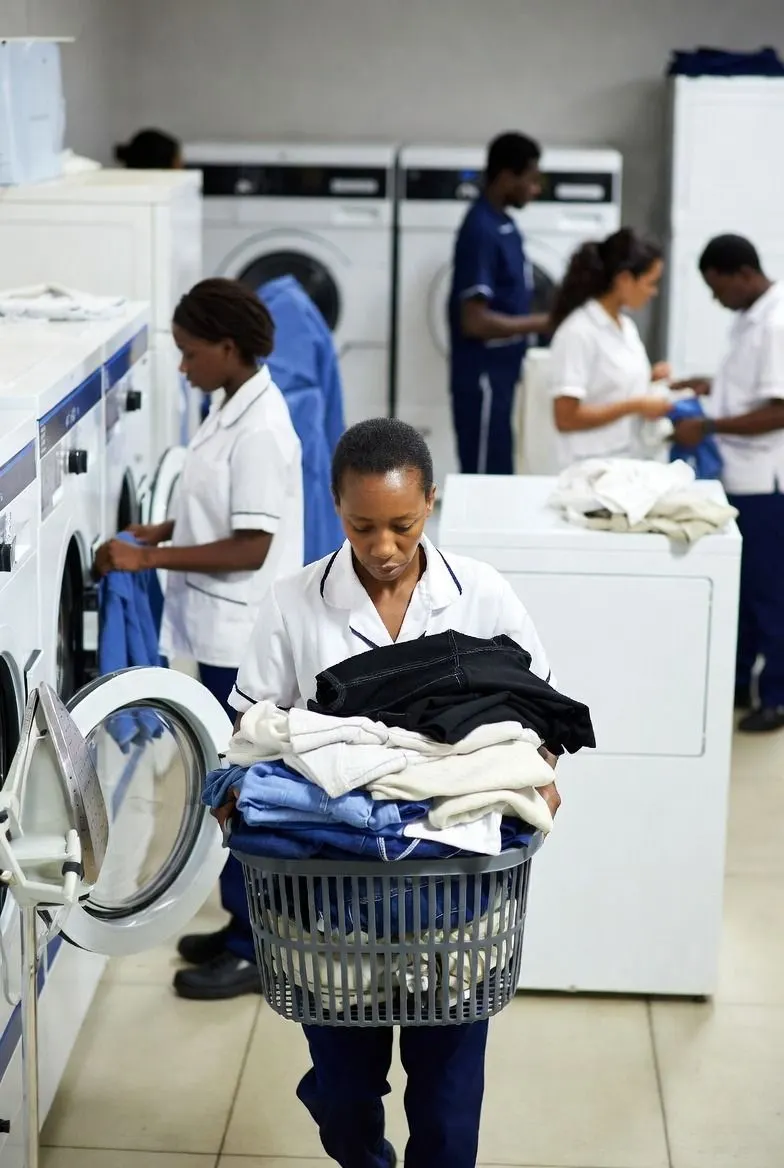 Laundry staff in uniform sorting and carrying linen in a commercial laundry room