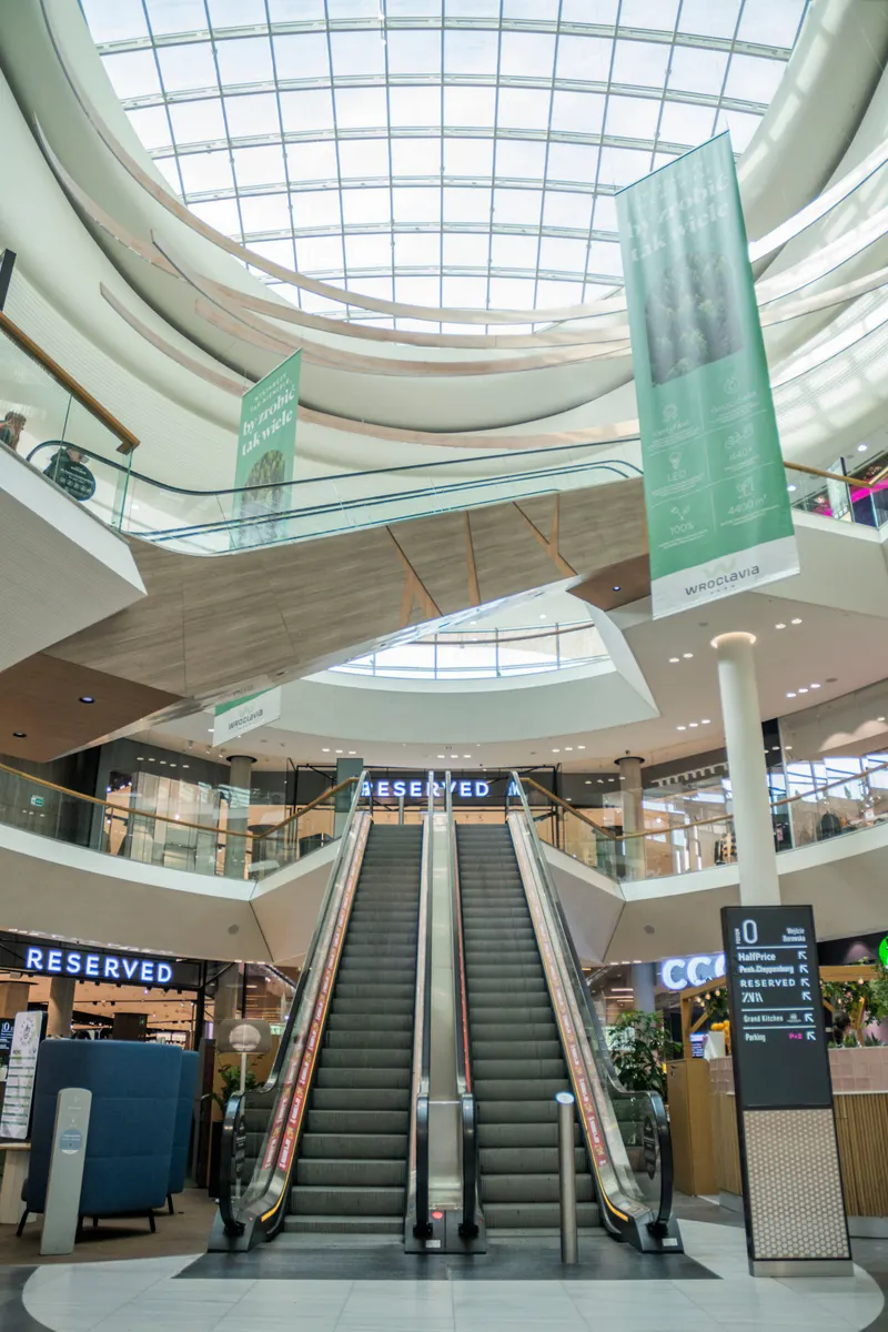 A bright shopping mall atrium with escalators under a glass roof